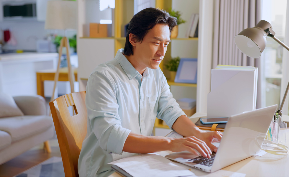 Asian man typing on laptop in home office